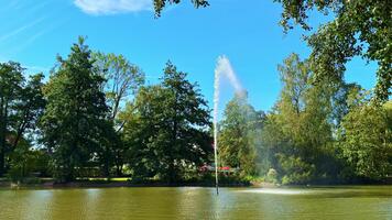 lugn parkera scen med en fontän skapande en gnistrande visa mot en klar blå himmel video