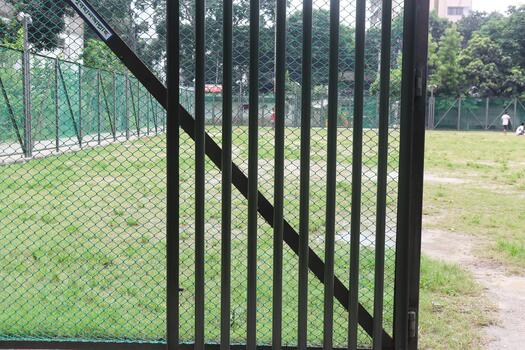 Closed metal gate with vertical bars and wire mesh fence in a grassy outdoor area photo