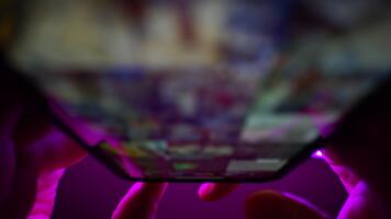 stänga upp av fingrar rörande och rullning på mobil Ansökan. på en lila neon toner bakgrund. internet bläddring, social media marknadsföring. suddig makro. topp se mörk skott video