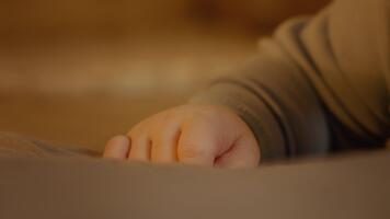 fechar-se tiro do uma pequeno gordo mão do uma bebê dentro dele primeiro ano do vida. criança vestido dentro macacão em a cama, médio tiro do dele mãos. puericultura e infância conceito. video