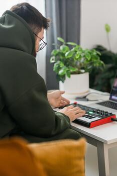 Male recording electronic music track with portable midi keyboard on laptop computer in home studio. Producing and mixing music beat making and arranging audio content photo