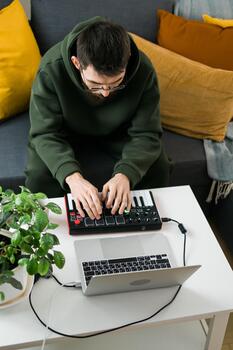 Top view Man recording electronic music track with portable midi keyboard on laptop computer in home studio. Producing and mixing music beat making and arranging audio content photo