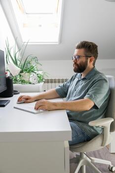 Man working at computer desk under skylight. Representation of focus, productivity, and modern remote work routine in bright home office environment. photo