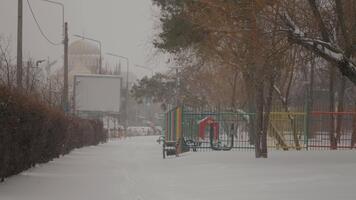 snö filtar en vibrerande lekplats, skapande en lugn vinter- landskap. barns gungor och diabilder titt genom de vit som snöflingor falla mjukt i de urban miljö. video