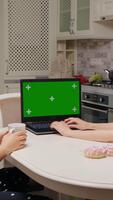 Vertical Screen Two female sit at a table in the kitchen in front of laptop with a green screen. Filming from the back, two collegues working from home. video