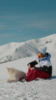 vertikal skärm caucasian kvinna med hund har resten efter gående på peaky berg. hund be för stängning medan Sammanträde med de ägare på snö. video