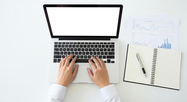 Hands typing on a laptop keyboard with charts and notepad on a desk photo