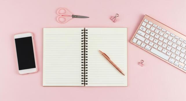 Flat lay of a modern workspace with a smartphone, keyboard, notebook, and scissors on a pink background photo