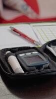 verticale schermo un' glucometro impostato lungo con medicazione e un' taccuino posto su un' tavolo. esso punti salienti il importanza di monitoraggio sangue zucchero livelli, registrazione dati video