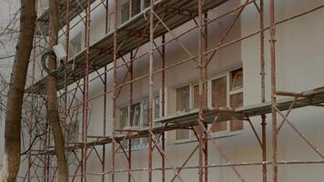An empty construction site features scaffolding surrounding a residential building undergoing insulation and rehabilitation. Workers are preparing for further development. video