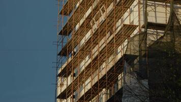 konstruktion aktiviteter är på gång som arbetare isolera en höghus byggnad omgiven förbi byggnadsställningar, förbättra dess termisk effektivitet och framställning för renoveringar. video