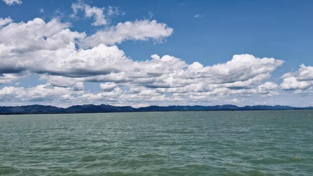 Expansive Ocean View Under a Cloudy Blue Sky with Distant Mountains photo