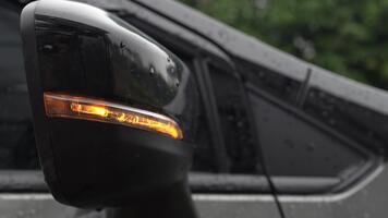närbild se av bil sida spegel med sväng signal ljus upplyst på en regnig dag med suddig bakgrund av grönska video