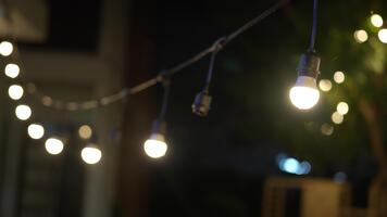 Cozy outdoor string lights illuminating a warm evening atmosphere in a garden or patio setting with blurred background and soft bokeh effect video
