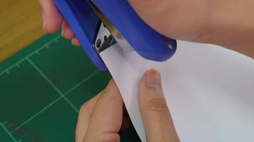 A person's hand holds a blank white sheet of paper above a green cutting mat, ideal for creative projects or artistic layouts in a workspace setting. video