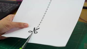 A close-up view of a hand holding scissors and cutting through paper, showcasing a dotted line as a guide. This image captures the essence of creativity and craft. video