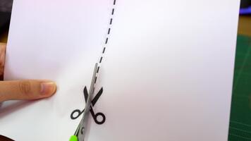 en hand innehav sax är skickligt skärande längs en prickad linje på en ark av vit papper. de arbetsyta inkluderar en skärande matta och olika skrivbord föremål, betona kreativitet. video