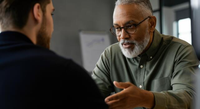 Man with glasses explaining something to another man in professional setting photo