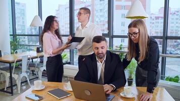 Active and busy working day in office. Boss in front of laptop and female standing next to him discussing issues in computer. Man and woman having discussion at the background. video