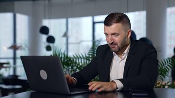 stilig affärsman bläddring internet på hans bärbar dator och tala. man i en kostym arbetssätt på dator i stor kontor. suddig bakgrund. video