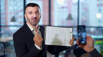 mano con un teléfono tomando de un hombre con cuadro. hermoso hombre demostración grafico patrones y explicando ellos a el cámara. video