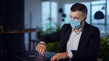 man i kostym sätta på mask medan Sammanträde på de tabell. affärsman öppnas och kläder bärbar dator, försöker till öppen den om igen och misslyckas. stänga upp. video