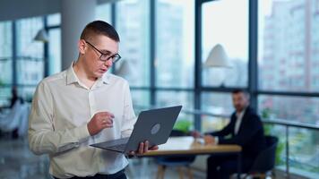 man i vit skjorta innehav en bärbar dator i hans hand. företag chef förklara något och som visar på hans dator. suddig bakgrund. video
