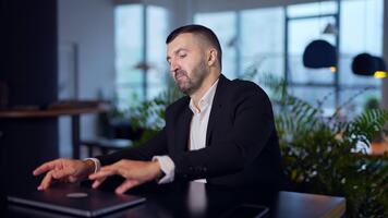 Man in suit sitting at the table and laptop in front of him. Bearded man trying to open computer but fail again and again. Blurred background. video