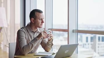 lugna avslappnad man sitta i främre av hans dator med en kopp i händer. omtänksam man utseende in i fönster och sedan hetero ett huvud. video