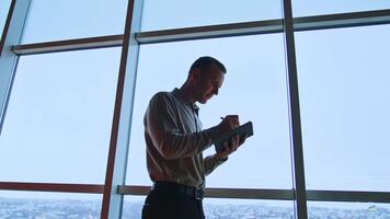 upptagen man tar anteckningar in i papper anteckningsbok. manlig arbetstagare står i främre av stor fönster och skrivningar i hans bok. låg vinkel se. video