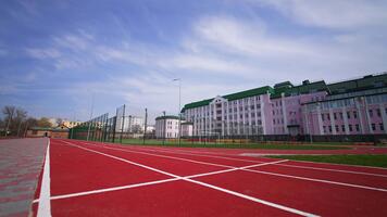Aproximando uma futebol campo cercado de cerca dentro frente do a grande Rosa prédio. vermelho corrida rastrear às a primeiro plano. baixo ângulo visualizar. video