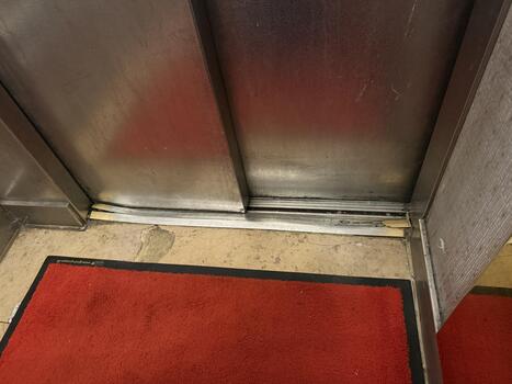 Worn elevator door with visible floor damage and red carpet in building entrance area photo