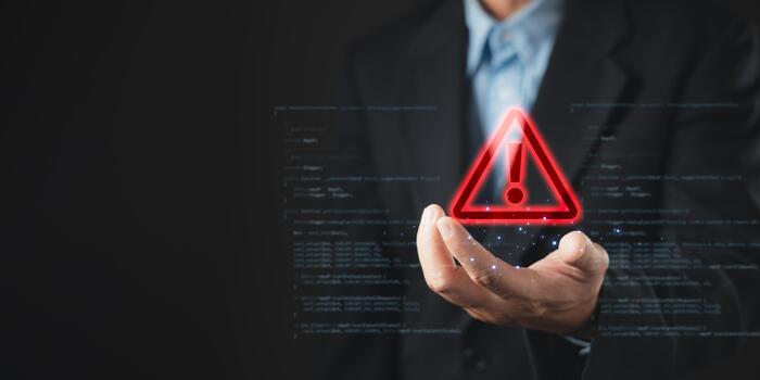 A businessman holds a glowing red warning triangle with an exclamation mark, symbolizing alert, caution, and cybersecurity threat in digital systems, with code elements in the background. photo