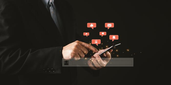 A person in a suit uses a smartphone as glowing red social media icons like, heart, location, message, alert float above, representing mobile engagement, notifications, and online interactions. photo