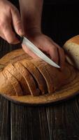 Hands are skillfully slicing a loaf of freshly baked bread on a wooden cutting board. The warm atmosphere highlights the texture of the crust and the soft inside of the bread. video