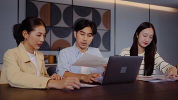 tre asiatisk individer förlova sig i en allvarlig diskussion på en tabell. varje person recensioner grafer och statistik visas på bärbar dator dator. i samarbete analyserar data med fokus och avsikt video