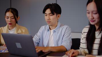 tre asiatisk individer förlova sig i en allvarlig diskussion på en tabell. varje person recensioner grafer och statistik visas på bärbar dator dator, i samarbete analyserar data med fokus och avsikt. video