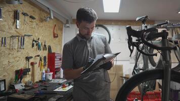 maschio bicicletta meccanico Lavorando con documenti, controllo qualità di completato Servizi nel bicicletta officina. ciclo tecnico mantiene Nota nel taccuino. ingegneria e mantenimento biciclette. video