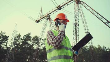 elettrico ingegnere è Lavorando. parlare su Telefono. controllo energia griglia. energia. industria. elettricità ingegnere sotto pilone parlando su Telefono e controllo dati su tavoletta con documenti di oggetto video