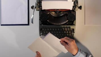händer framställning sändning en personlig meddelande, införing en skriven brev in i en enkel kuvert Nästa till ett gammal mekanisk skrivmaskin, förkroppsligande årgång kommunikation begrepp video