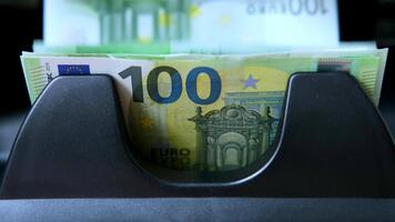 Close-up bundle of 100 euro banknotes moving in currency counting machine. Bills are showing security features, vibrant green and yellow color. Financial transactions and money handling concept video