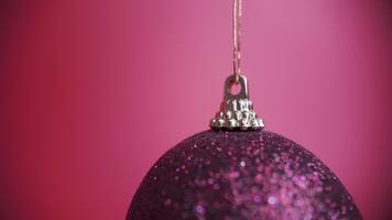 lento movimento avvicinamento di un' glitterato Natale ornamento delicatamente ondeggiante nel un' statico telaio, catturato con un' macro lente su rosso sfondo video