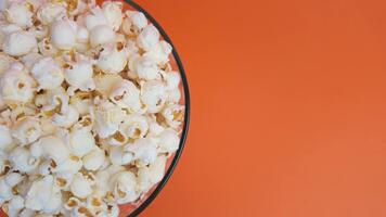 roterande glas skål full av popcorn på orange yta, långsam rörelse studio skott som visar rörelse, textur, och aptitlig Färg video
