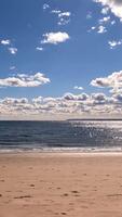 Timelapse of a sunny beach with sparkling ocean waves, Calm sandy beach with sparkling ocean waves under a bright sunny sky and fluffy clouds video