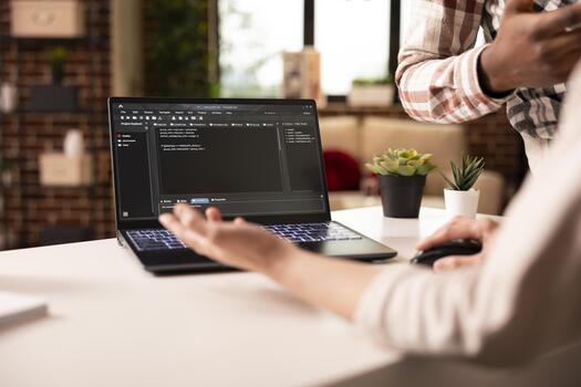 Closeup on laptop displaying programming language as multiethnic people discuss on building an app from home. Diverse couple brainstorming and debugging code for web development in modern apartment. photo