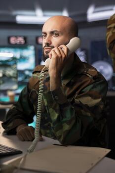 Officer in command center responsible for air defense relaying instructions to squadrons patrolling over borders using phone. Military intelligence agent alerting troops during phone call photo