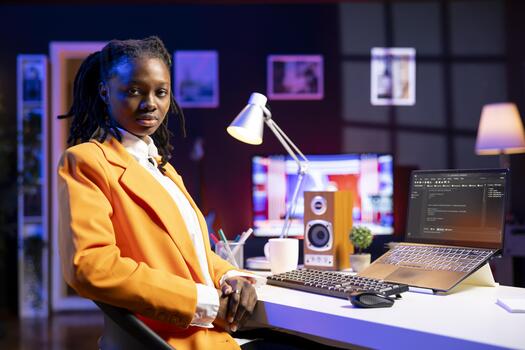 Portrait of programmer at desk typing code on laptop, developing software programs, entering commands. African american woman at home fixing errors in application, implementing new features photo