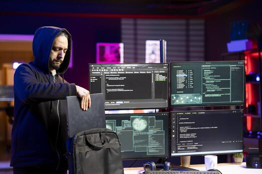 Hacker packing laptop after finishing coding stealth malware to evade security. Evil man putting notebook in backpack after finishing work on script hiding malicious code from detection systems photo