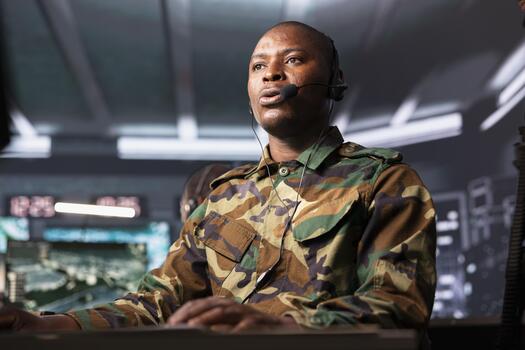 Army telecommunication systems operative in command post using radio and satellite gear, providing combat support using headset mic. Soldier managing communications networks from control room photo