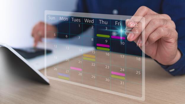 A calendar with a calculator for calculating monthly income and expenses for employees or individuals. A man using a digital pen is working on a virtual holograph icon at a desk in an office. photo